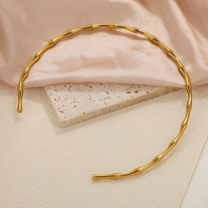 Minimalist gold bamboo style choker necklace with metallic luster on silk background