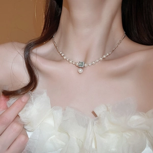Close-up of pearl necklace with square green gemstone and dangling teardrop pearl detail