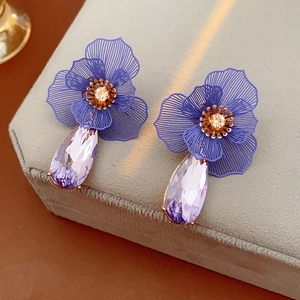 Detailed macro view of purple flower earrings with teardrop crystal charms on a velvet stand