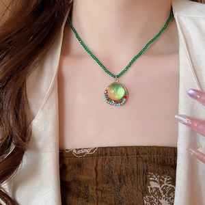 Detail of vintage round pendant with green gemstone and colorful beads on model neck
