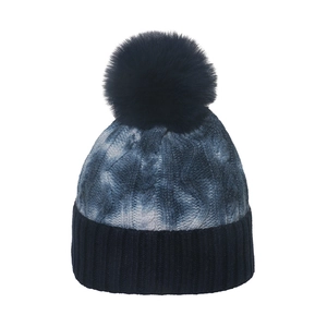 Detail of chunky cable knit pattern and fluffy faux fur pom-pom on navy blue beanie