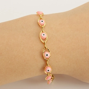 Golden Evil Eye link bracelet with pink enamel charms worn on a female wrist