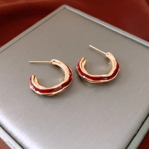 Macro detail of gold-plated C-shaped earrings with red enamel and lava texture