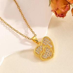 Dettaglio della collana con doppio ciondolo a cuore dorato e cristalli su sfondo elegante
