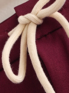 Detailed macro view of heavy beige drawstring knot on wine red fabric textured material