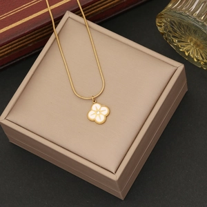 Detail of gold clover pendant with sunburst engraving on a beige jewelry box