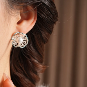 Close-up of hollow flower stud earrings with a white pearl and blue enamel finish