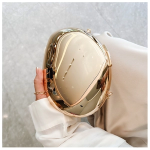 Macro shot of oval gold metal hardshell clutch with mirror finish and chain strap