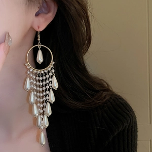 Detail of long gold tassel earrings with teardrop pearls and sparkling zircons on model