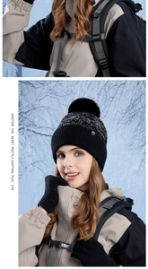 Close-up of black knit beanie with faux fur pom and matching touch screen gloves in snow