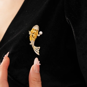 Detailed close-up of golden carp brooch with yellow gems and pearl on black velvet