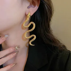 Elegant gold snake drop earrings with green gemstone eyes on female model profile
