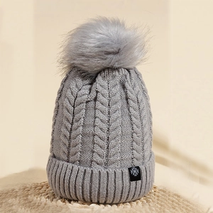 Close-up of gray cable-knit beanie featuring a fluffy pompom and snowflake logo patch