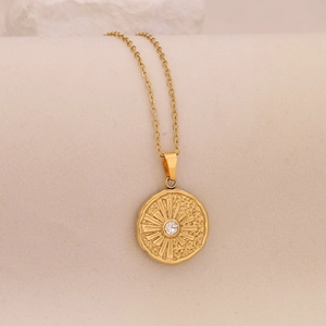 Detail of gold starburst necklace with central clear gem on subtle beige texture