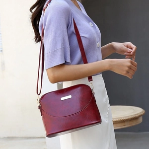 Detail of burgundy glossy leather crossbody bag with gold hardware worn by a model