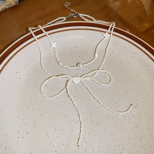 Detail shot of a layered beaded necklace with bow, pearls and star charms in a ceramic plate