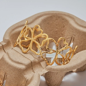 Macro shot of gold hollow flower bangle with intricate clover patterns on craft tray