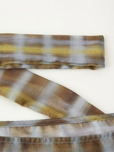 Macro detail of tan and blue plaid tie-dye fabric showing rolled hem and sheer texture