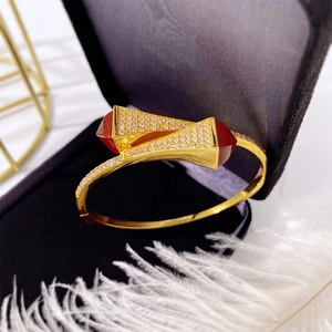 Detail of golden open bangle featuring red agate triangles and sparkling diamond accents