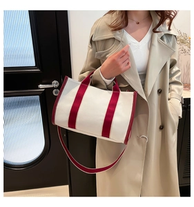 Detail view of canvas tote bag with red handles and detachable shoulder strap on model