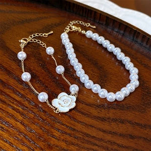 Macro shot of French vintage pearl bracelets with enamel camellia charms on wood