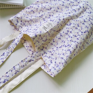 Detail of floral canvas tote bag with purple patterns and white strap on wooden table