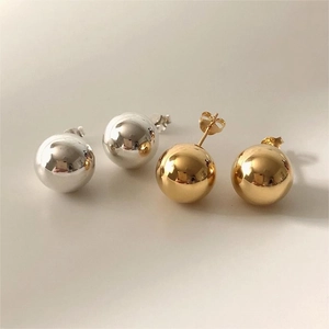 Macro detail of minimalist spherical stud earrings in polished silver and gold finishes
