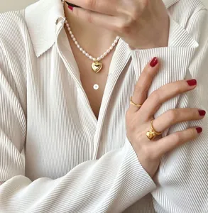 Close-up of elegant pearl necklace with gold heart pendant and matching rings on a model