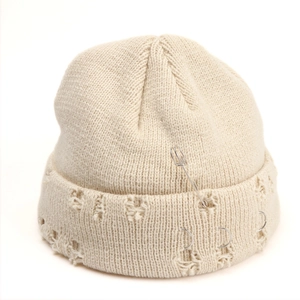 Detail of beige knit beanie with silver safety pin, metal rings and distressed holes