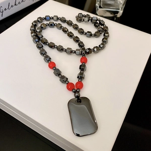 Macro detail of dark grey bead necklace with polished metal dog tag on white box