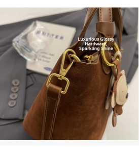 Detail der braunen Wildleder-Eimertasche mit Goldbeschlägen und Bärenanhänger