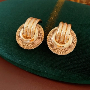 Close-up of golden mesh hollow round stud earrings on dark green velvet background