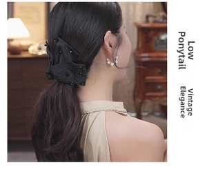 Close-up of a vintage black satin bow hair clip with sequins worn on a low ponytail