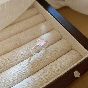 Detailed close-up of a pink opal ring with crown setting on a linen display box