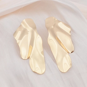 Macro view of gold irregular wavy geometric metal stud earrings on silk fabric