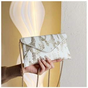 Close-up of white envelope chain bag with golden crocodile pattern and metallic strap