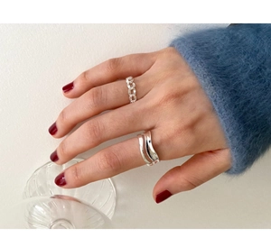 Close-up of minimalist silver wave and chain ring set worn on finger with a chic blue sweater