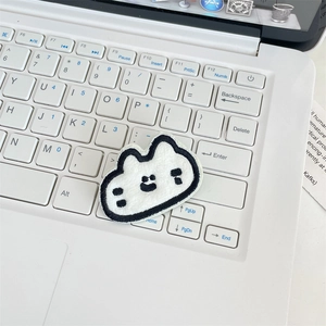 Detailed macro view of white plush cartoon cat embroidery patch on a laptop keyboard