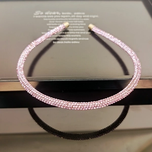 Detail of pink rhinestone headband with gold metal ends on a black reflective surface