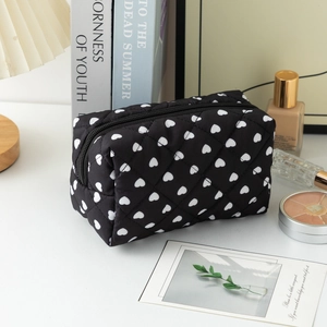 Detailed view of black quilted makeup bag with white hearts in a cozy lifestyle setting
