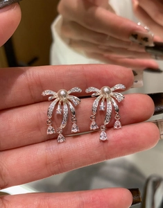 Detail of silver bow earrings with pearl and long tassel fringe featuring zircon accents