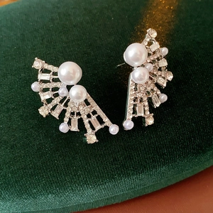 Macro detail of fan-shaped earrings with pearls and rhinestones on green velvet