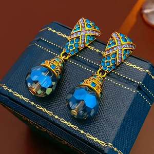 Macro shot of vintage gold drop earrings with blue crystals on dark leather box
