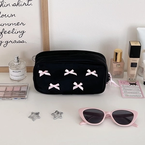 Detail of black fabric makeup bag with pink bows and ribbon zipper in a lifestyle set
