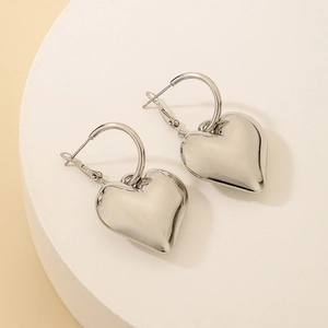 Macro detail of high-shine silver heart hoop earrings on a minimalist white platform