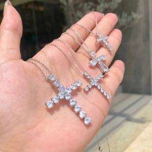 Detailed view of four silver cross pendants with shimmering zircon stones in hand