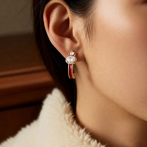 Detail of 18k gold-plated gourd earring with red enamel and clear zircons on a model