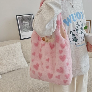 Pink plush heart pattern tote bag worn on shoulder in a cozy home setting