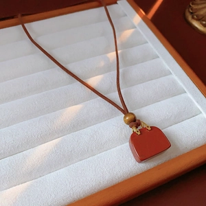 Detail of red bag pendant necklace with brown leather strap on white velvet tray