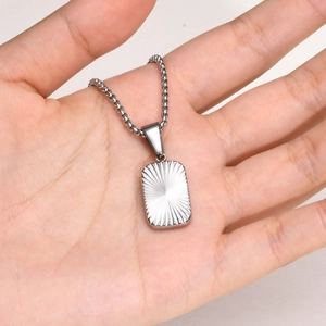 Macro shot of a silver rectangular stainless steel pendant with radiant texture on a chain